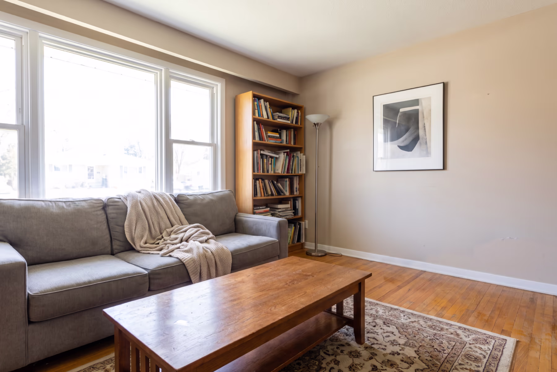 The same room after Declutter Room: the sofa, coffee table and floor are clear, and the sofa, knit throw, coffee table, rug, bookcase, floor lamp and framed print are where they were.